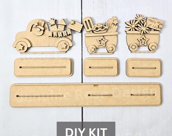 May include: A DIY kit featuring wooden cutouts of a truck, carts, and stands. The truck carries fireworks and a banner that says "USA". The carts hold ice cream, cupcakes, and flowers. The text "Happy 4th of July" is visible.