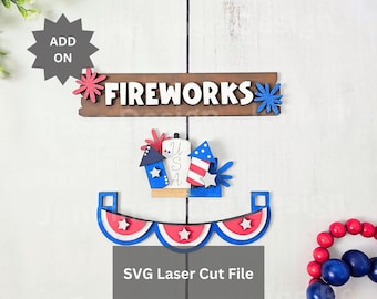 May include: A wooden sign with the text FIREWORKS in white letters, featuring red and blue starburst accents. Below, a patriotic cutout displays the letters USA with rocket motifs, and a scalloped banner with red, white, and blue layers.