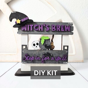 May include: A Halloween-themed DIY kit featuring a witch's hat, a sign that reads "Witch's Brew", a skull, and a cauldron with green bubbling liquid. The sign also says "Stop in for a spell". The kit is on a white and black stand.