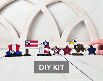 May include: A DIY kit featuring patriotic wooden cutouts including a top hat, a flag, a block with the text USA, three stars in various patterns, and a bald eagle. Each piece is painted in red, white, and blue, and stands on a small base.