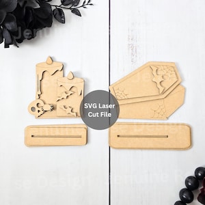Puede incluir: Decoraciones de Halloween de madera cortadas con láser. Incluye formas de velas, murciélagos, calaveras y ataúdes. El texto "SVG Laser Cut File" es visible en una pegatina circular. Las decoraciones están sin terminar.