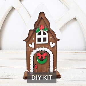 May include: DIY gingerbread house kit with a white roof, brown walls, a white door with a red bow and a green wreath, and a white window. The kit includes all the pieces needed to assemble the house.  DIY KIT.
