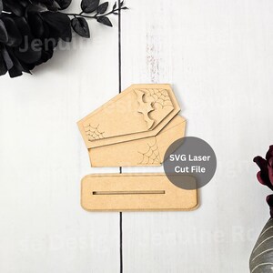 Puede incluir: Decoraciones de madera cortadas con láser en forma de ataúd con detalles de telarañas y murciélagos. Incluye una base para exhibición. El texto "SVG Laser Cut File" es visible. Ideal para manualidades de Halloween o de temática gótica.