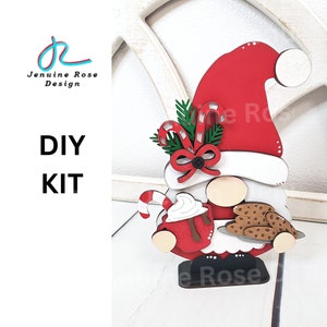 May include: DIY kit for a Christmas gnome with a red hat, white beard, and holding a red mug with whipped cream and a candy cane. The gnome is also holding a plate of chocolate chip cookies.