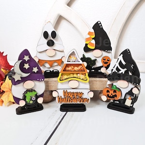 May include: Five Halloween gnomes with different themes. A ghost gnome, a candy corn gnome, a witch gnome, a black cat gnome, and a pumpkin gnome. The gnomes are all made of wood and painted in various colors. The candy corn gnome has a sign that says "Happy Halloween".