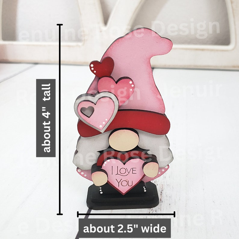 Puede incluir: Una figura de gnomo de madera para el D&iacute;a de San Valent&iacute;n que sostiene un coraz&oacute;n que dice "Te amo". El gnomo est&aacute; pintado de rosa, rojo, blanco y negro. Mide aproximadamente 10 cm de alto y 6,5 cm de ancho.