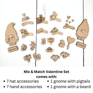 Puede incluir: Un conjunto de suministros de artesan&iacute;a de gnomos de madera para el D&iacute;a de San Valent&iacute;n. El conjunto incluye dos gnomos, uno con trenzas y otro con barba, junto con siete accesorios para sombreros, siete accesorios para manos y varias otras decoraciones con tem&aacute;tica del D&iacute;a de San Valent&iacute;n. El texto de la imagen dice "Mix & Match Valentine Set comes with: 7 hat accessories, 1 gnome with pigtails, 7 hand accessories, 1 gnome with a beard."