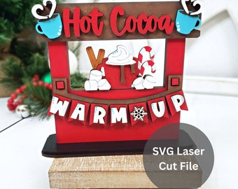 Könnte beinhalten: Ein hölzerner, rot-brauner Hot-Cocoa-Stand mit den Worten "Hot Cocoa" und "Warm Up". Der Stand zeigt blaue Tassen, Marshmallows, einen Zimtstange und Zuckerstangen. Der Stand steht auf einem Holzsockel mit kleinen, runden Füßen.