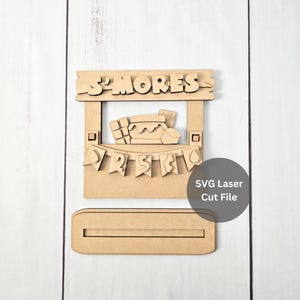 Puede incluir: Un letrero de madera cortado con láser con la palabra "S'MORES" en la parte superior. El letrero presenta una pancarta con los números "25" y un gráfico de un s'more. Incluye una base y el texto "SVG Laser Cut File".