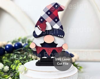 May include: A decorative gnome figurine featuring a tall hat with a red, white, and blue plaid pattern and white stars. The gnome has a round peach-colored nose, a white beard, and holds a red banner with the letters U, S, and A printed on it.