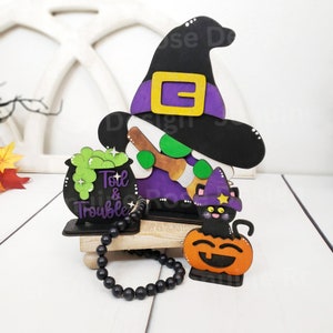May include: A wooden Halloween decoration featuring a witch with a black hat, a cauldron with green liquid, and a black cat sitting on a pumpkin. The cauldron says "Toil & Trouble".