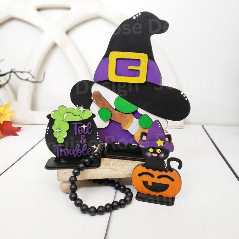 May include: A wooden Halloween decoration featuring a witch with a black hat, a cauldron with green liquid, and a black cat sitting on a pumpkin. The cauldron says "Toil & Trouble".