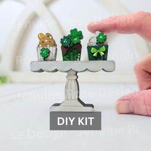 May include: DIY kit for a three-tiered cupcake stand with three wooden cupcakes decorated with green shamrocks and the word "Lucky".