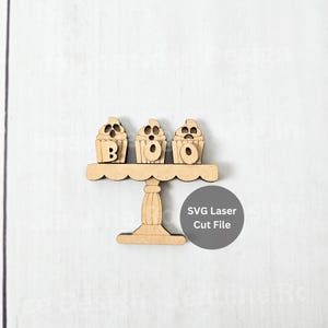 May include: A wooden cupcake stand with three cupcakes spelling "BOO". The cupcakes have a spooky design. The stand is made of light brown wood and has a scalloped edge. The text "SVG Laser Cut File" is in a grey circle.