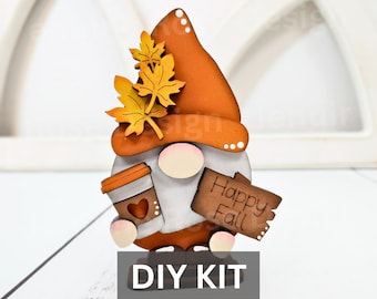 May include: DIY craft kit featuring a wooden gnome holding a coffee cup and a sign that says "Happy Fall". The gnome is painted in orange, white, and brown. The gnome has a hat with leaves on top.