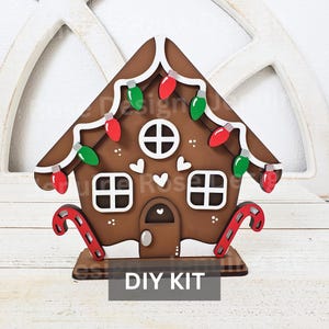 May include: A DIY gingerbread house kit with a brown wooden base, white icing details, and red and green candy decorations. The kit includes candy canes and a sign that reads "DIY KIT".
