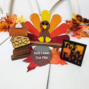 Puede incluir: Recortes de madera con temática de Acción de Gracias. Se muestra un pavo con plumas de cola coloridas, tres rebanadas de pastel apiladas y un letrero cuadrado que dice "let's talk turkey". Los recortes están rodeados de hojas de otoño.
