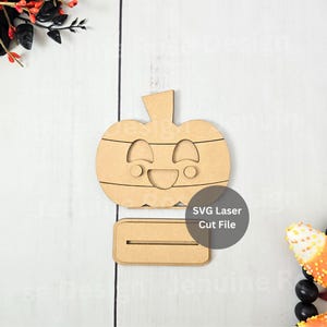 May include: A wooden pumpkin-shaped decoration with a smiling face and horizontal stripes. It includes a separate base with a slot. The text "SVG Laser Cut File" is visible. Ideal for Halloween or autumn decor.