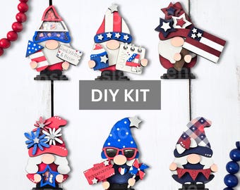 May include: Six wooden gnome ornaments featuring red, white, and blue patriotic themes. The gnomes include accessories like a rocket, a calendar marked July 4, a flag, stars, sunglasses, and a banner. The text reads Red, White & Boom and Happy Independence Day.