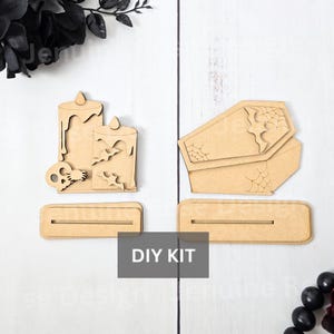 May include: DIY Halloween kit featuring wooden cutouts of candles, bats, a skull, and coffins. Each cutout has a slot for a base. The kit includes the text "DIY KIT" in a white box.