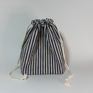 May include: A fabric drawstring bag featuring a navy and white striped design. It has a white drawstring closure. The bag is a simple, yet stylish accessory, suitable for various uses.