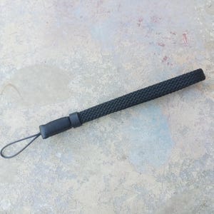 May include: A black camera strap with a braided design and a loop at one end.