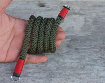 Könnte beinhalten: Ein grünes und rotes Kameraband aus geflochtenem Seil mit Metallringen an jedem Ende.