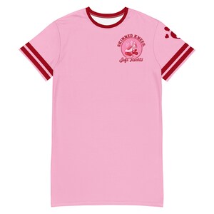 May include: Pink t-shirt with red and white striped sleeves. The shirt has a red circle graphic with the text "Skinned Knees, Soft Hearts" and a pair of roller skates.