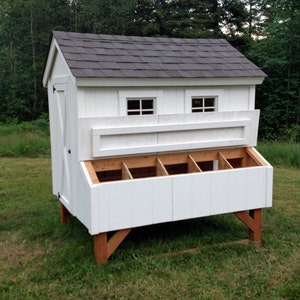 May include: White wooden chicken coop with a black shingled roof, two windows, and a nesting box with five compartments. The coop is raised on four wooden legs.