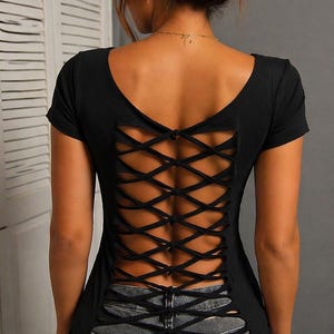 May include: Black short-sleeve top with a unique crisscross design on the back. The top has a scoop neckline and is paired with gray denim jeans. The back of the top features a lattice-like pattern.