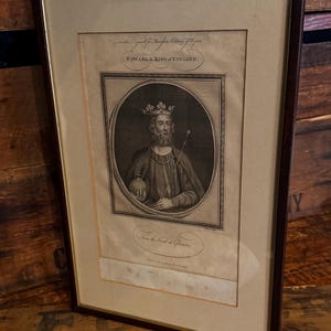 May include: Framed antique print of Edward II, King of England, in a dark wood frame. The black and white portrait shows the king wearing a crown and holding a scepter and orb. The print includes text at the top and bottom.