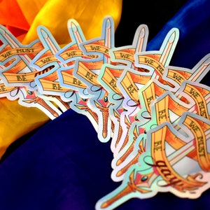 May include: A stack of iridescent stickers featuring a sword and a banner with the text "We must be brave".