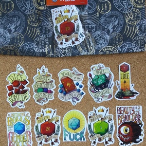 Puede incluir: Un conjunto de diez pegatinas con temática de Dungeons and Dragons que presentan dados, monstruos y frases humorísticas. Las pegatinas están impresas en papel blanco con ilustraciones y texto coloridos. Las pegatinas están empaquetadas en una bolsa de plástico transparente.