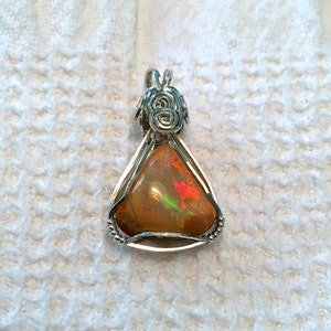 May include: A silver wire wrapped pendant featuring a triangular orange opal gemstone with iridescent flashes of green and red.