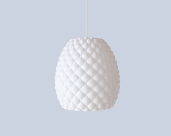May include: A white, pendant light fixture with a textured, diamond-patterned shade. The light hangs from a white cord against a pale blue background. The shade has a rounded, elongated shape.