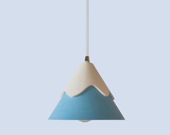 May include: A blue and white pendant light shaped like a mountain. The light has a white top and a blue bottom with a wavy edge.