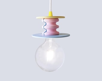 May include: A pendant light fixture featuring a clear globe bulb suspended from a white cord. The fixture includes a yellow circular top disc, a central pink cylindrical component with three horizontal ridges, and a light blue circular base disc.