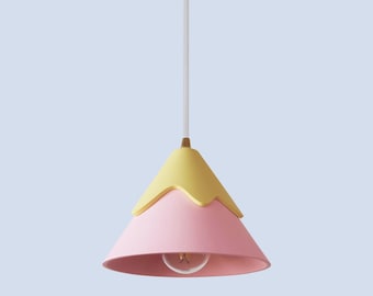 May include: A pink and yellow pendant light shaped like a mountain. The light has a white cord and a clear light bulb.