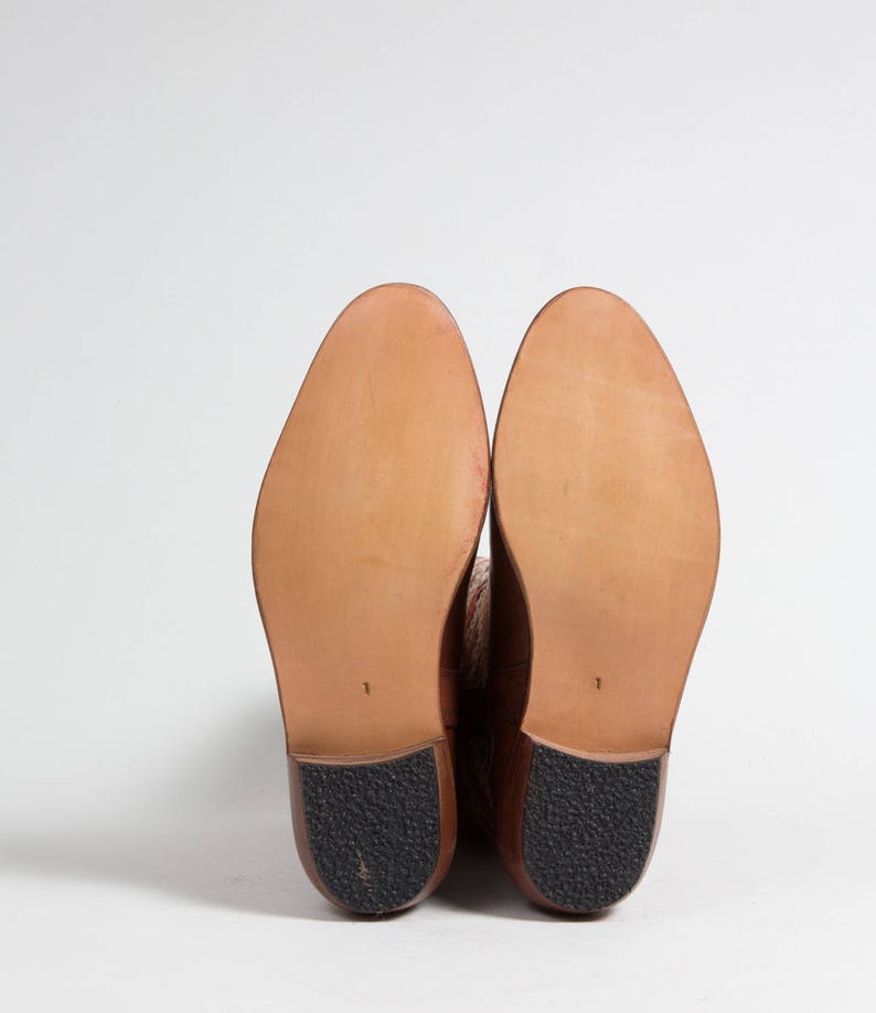 May include: A pair of brown leather knee-high boots with a brown leather sole. The boots are shown from the bottom, with the soles facing the camera.