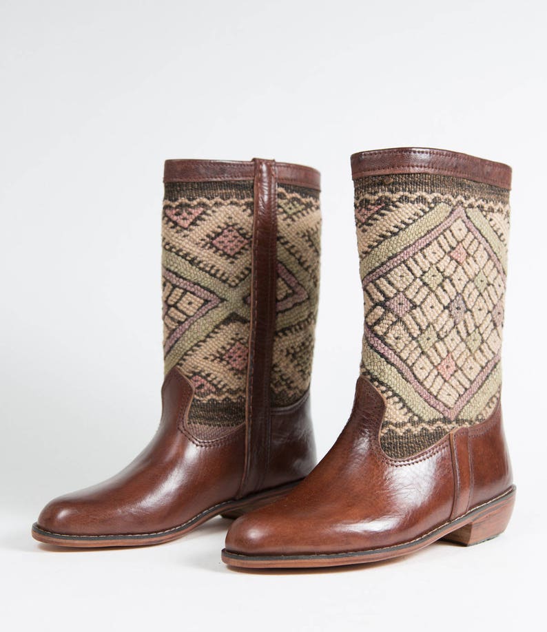 May include: A pair of brown leather boots with a geometric patterned fabric shaft. The boots have a pointed toe and a low heel.