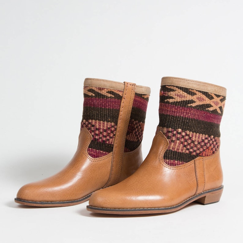 May include: A pair of tan leather ankle boots with woven fabric shafts. The fabric features a geometric pattern in shades of burgundy, brown, and tan. The boots have a low heel and a side zipper.