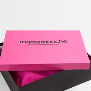 May include: A pink box with a black logo that says "mamawouche" and "Chaussures artisanales marocaines 100% cuir". The box is open and the inside is lined with pink fabric.