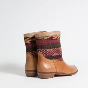 May include: A pair of tan leather ankle boots with woven fabric shafts. The fabric features a pattern of burgundy, brown, and tan geometric designs. The boots have a low heel and a rounded toe.