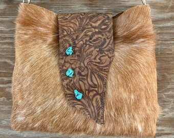 May include: A brown leather handbag with a long strap and a flap with turquoise accents. The bag is made of cowhide and has a unique, embossed design.