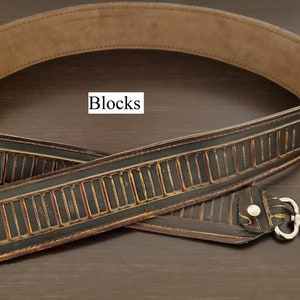 May include: A black and brown leather bag strap with a repeating rectangular design and silver-coloured clasps. The strap has a light brown interior and the word "Blocks" is in a white box.
