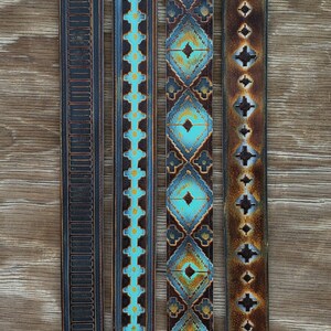 May include: Four leather straps with decorative designs and silver-coloured clasps. The straps feature embossed patterns and turquoise, brown, and black colour schemes. The straps are displayed on a wooden surface.