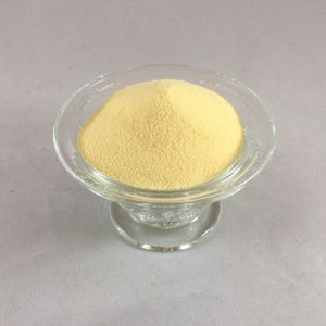 May include: A small glass bowl filled with a mound of pale yellow powder.