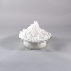 以下が含まれることがあります： 白い粉末がたっぷり入った透明なガラスボウル。粉末はきめ細かく、食品成分または化粧品のように見えます。ボウルは、無地の明るい灰色の背景に置かれています。