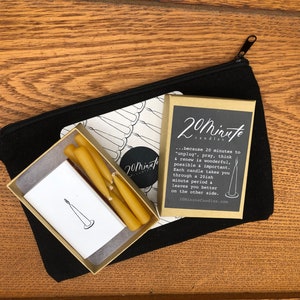 May include: A set of six small, yellow beeswax candles in a white box with a black and white illustration of a candle. The box is inside a black zippered pouch. The box is labeled "20 minute candles" and includes the text "...because 20 minutes to "unplug, pray, think & renew is wonderful, possible & important. Each candle takes you through a 20ish minute period & leaves you better on the other side. 20MinuteCandles.com"