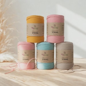 May include: Six spools of macrame string in shades of yellow, pink, light blue, and beige. Each spool has a brown label with the text "Macrame STRING". The spools are stacked on a light brown wooden surface. Ideal for crafting.